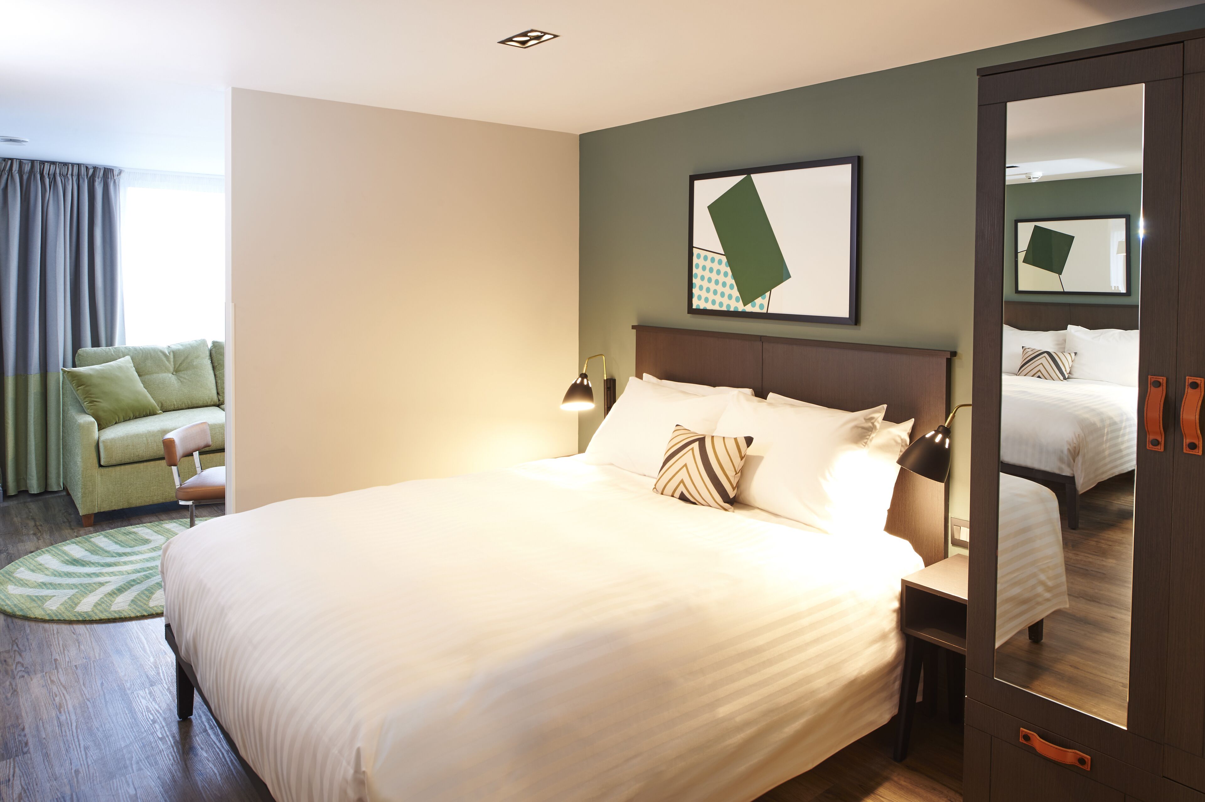 Een verzorgde hotelkamer met een groot bed, een stoel, een bureau en een spiegel.