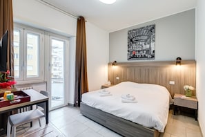 Una habitación de hotel moderna con una cama, un escritorio con bandeja, una silla, una mesita y una mesita de noche con lámpara.