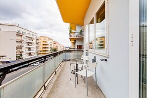 A balcony with a glass railing overlooking a street, a small table, and two chairs. - B&B Casa Der Poeta (Rome)