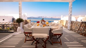 A covered outdoor dining area with a table set for two, overlooking a scenic coastal view. - Adelante 88 (Santorini)