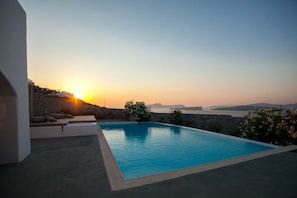 A swimming pool with a sunset view, a stone wall, and a seating area with cushions.