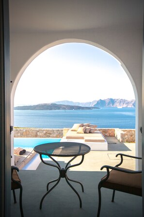 An outdoor seating area with a table and chairs, overlooking a pool and a scenic view of the sea and mountains. - Adelante 88 (Santorini)