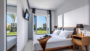 Una habitación de hotel moderna con una cama grande, televisión, mesita de noche con lámpara y vistas al exterior.