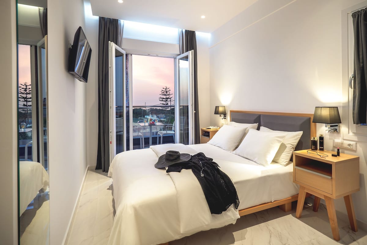 A modern hotel room with a large bed, bedside tables with lamps, a TV, and a balcony with a city view.
