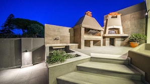 Un patio exterior moderno con una estructura de hormigón, una parrilla empotrada y escalones que conducen a una zona de estar.