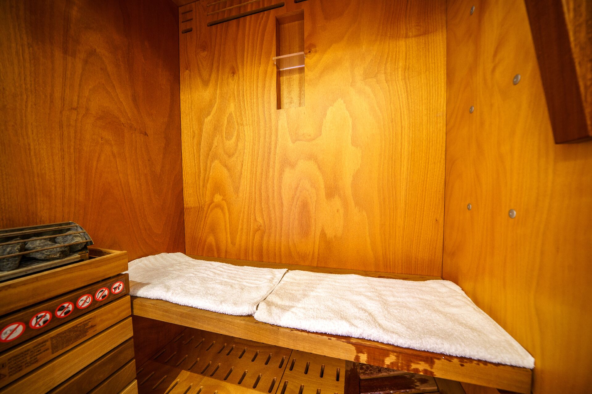 A sauna with wooden walls and benches, a towel on the bench, and a window.