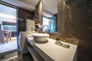 A modern bathroom with a large mirror, a vessel sink, and a countertop with toiletries. - Elysian Suites (Hersonissos)