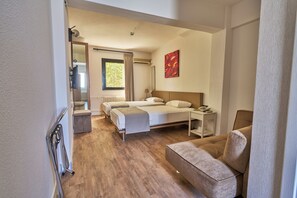 Habitación de hotel con cama, mesita de noche con teléfono, una silla, una pequeña mesa y ventana con cortinas.