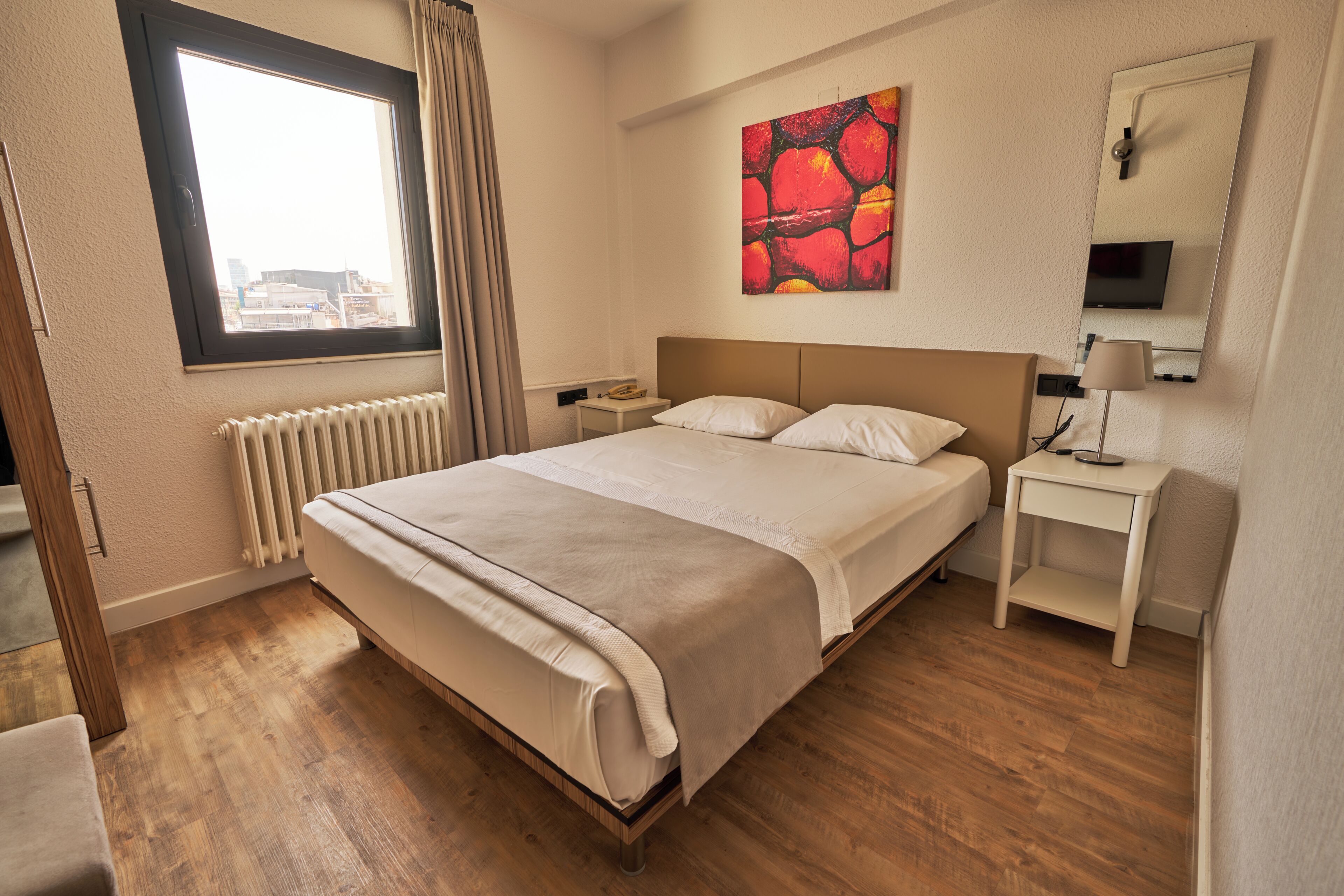 A hotel room with a bed, a nightstand, a lamp, a painting, and a window with curtains.