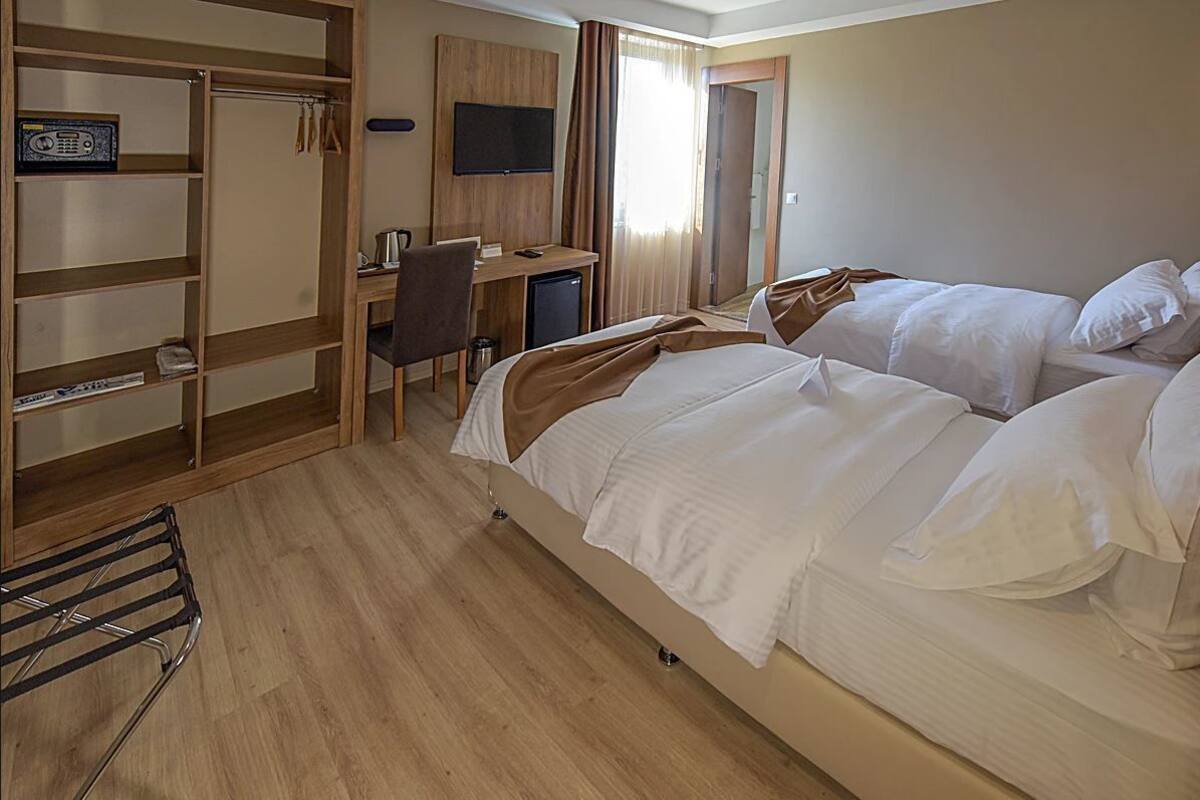 A hotel room with two beds, a desk, a chair, a TV, and a wardrobe.