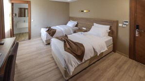 A hotel room with two beds, a wooden floor, a bedside table, a mirror, a small desk, and a bathroom visible through an open door. - Otel Vona Ordu (Ordu)