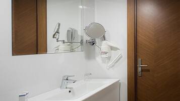 A bathroom with a white sink, a mirror, and a hairdryer mounted on the wall.