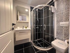 Een moderne badkamer met een douchecabine van glas, een toilet en een wastafel met een spiegel erboven.