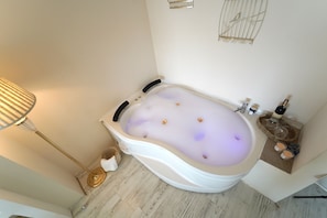 A modern bathroom with a freestanding bathtub, a floor lamp, and a small shelf with candles and a bottle.