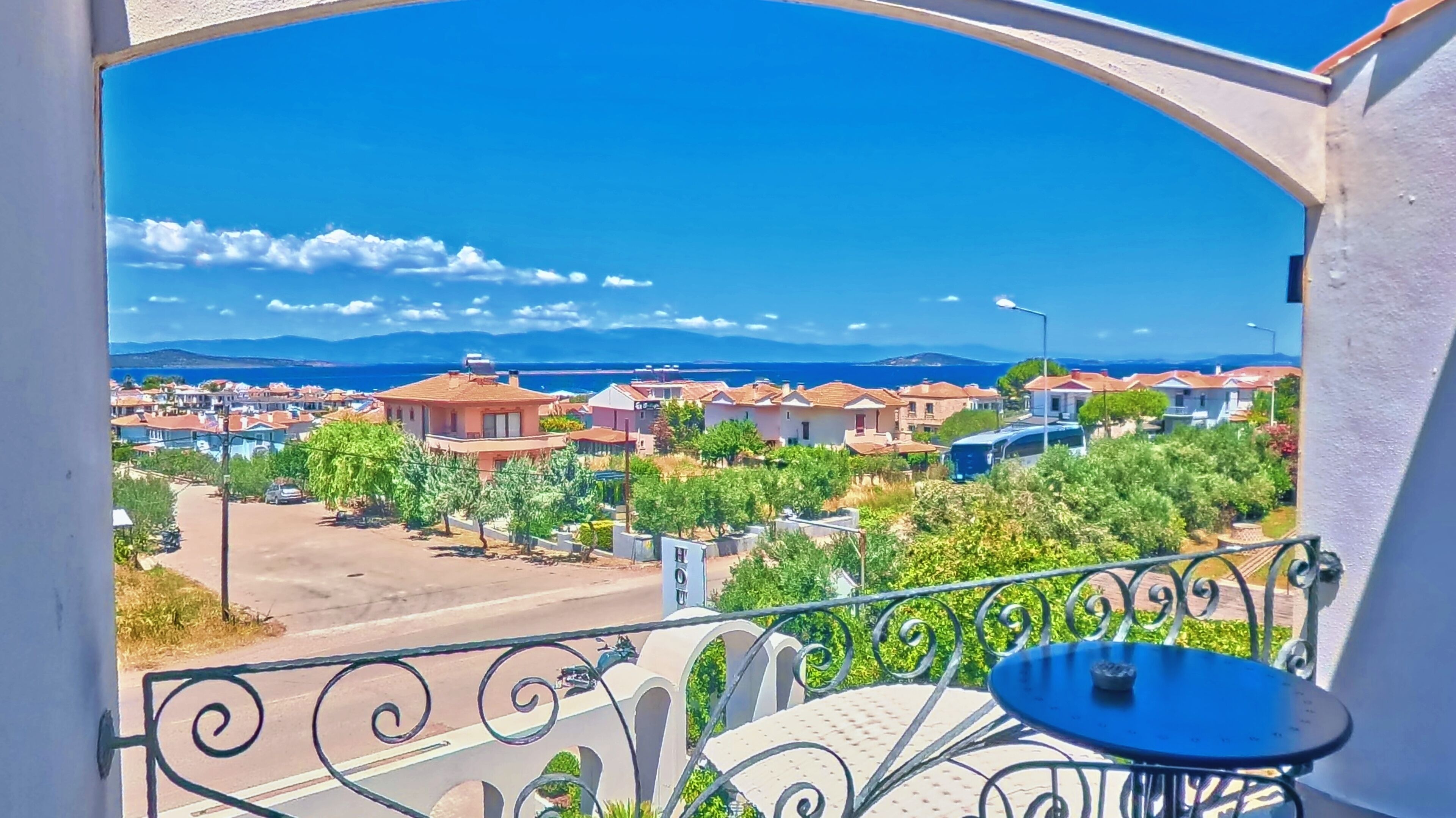 A balcony with a view of a coastal town, a table, and a chair.