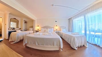 Habitación de hotel con dos camas, un área de descanso, un ventanal con cortinas y un espejo en la pared.