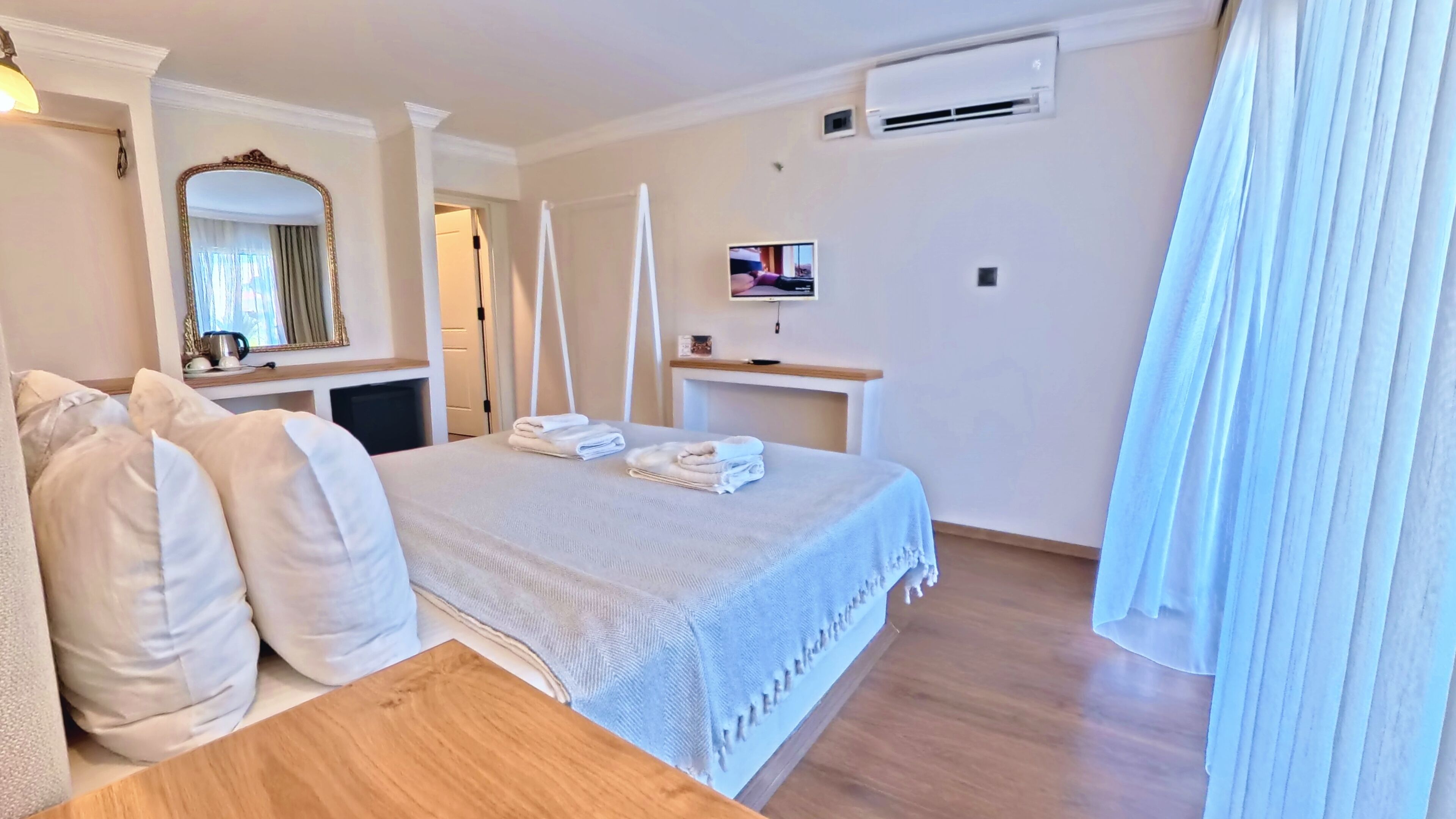 Habitació d'hotel amb un llit, una taula de nit, un mirall, un televisor i un aparell d'aire condicionat.