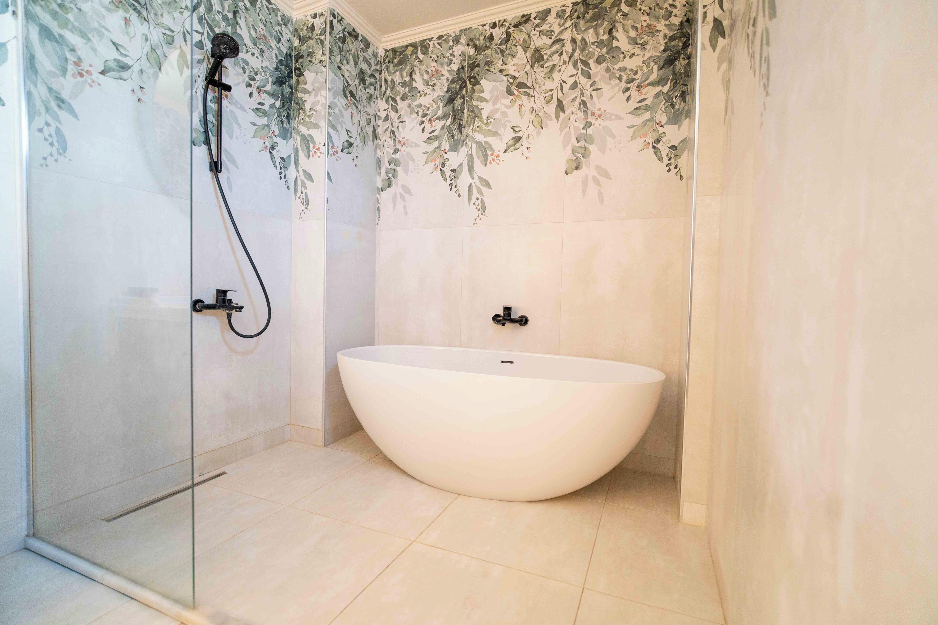 Un baño con bañera independiente, cabina de ducha de vidrio y azulejos florales.