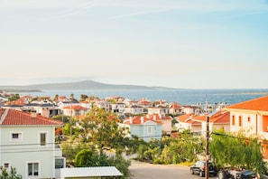 A coastal residential area with houses, a visible road, and a distant view of the sea and mountains.