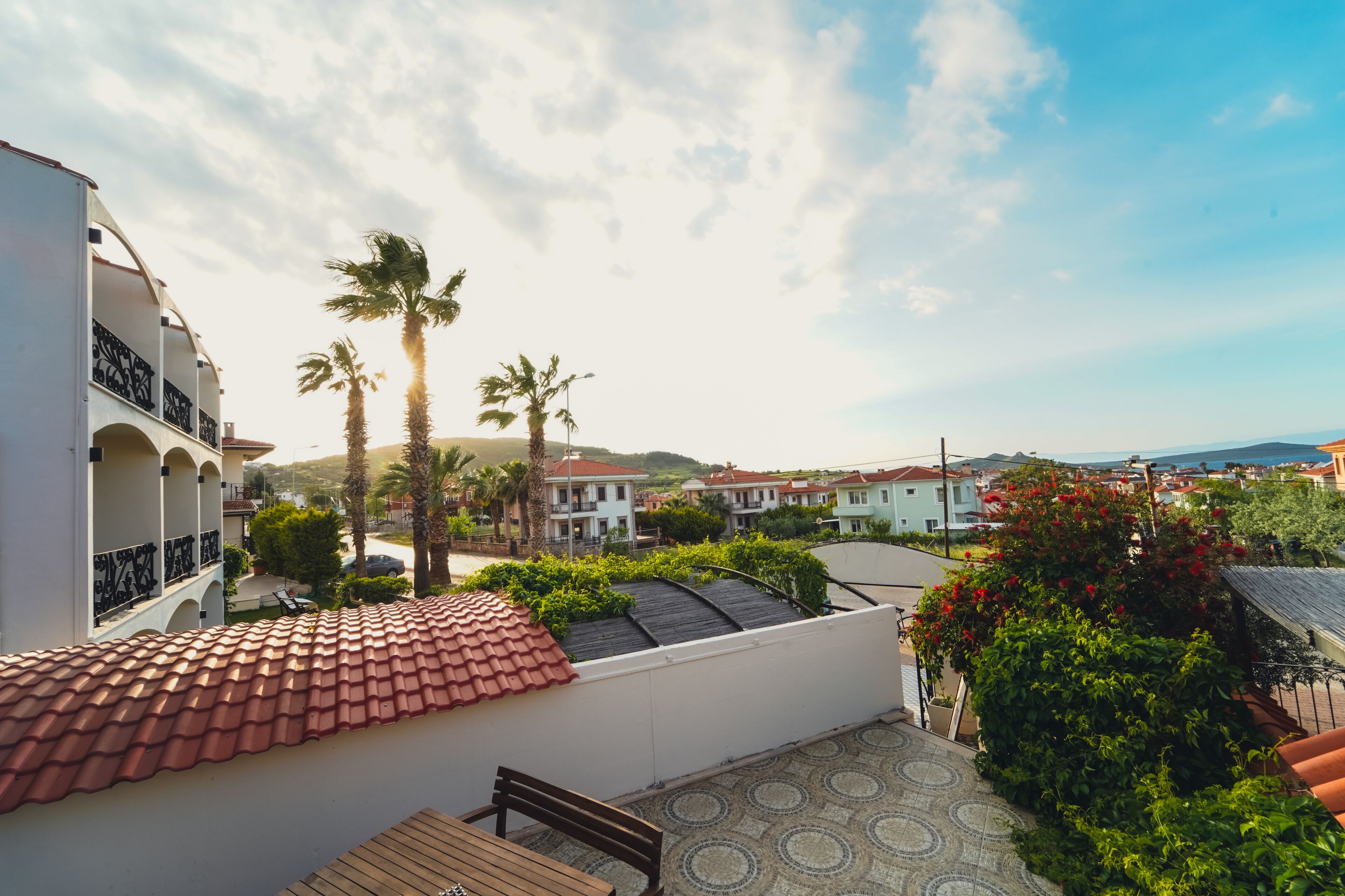 Una terraza en la azotea con techo de tejas, un banco de madera y vistas a una zona residencial con casas y palmeras.