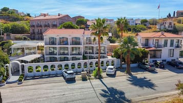 A multi-story hotel with a white facade, balconies, and a parking area with several cars.