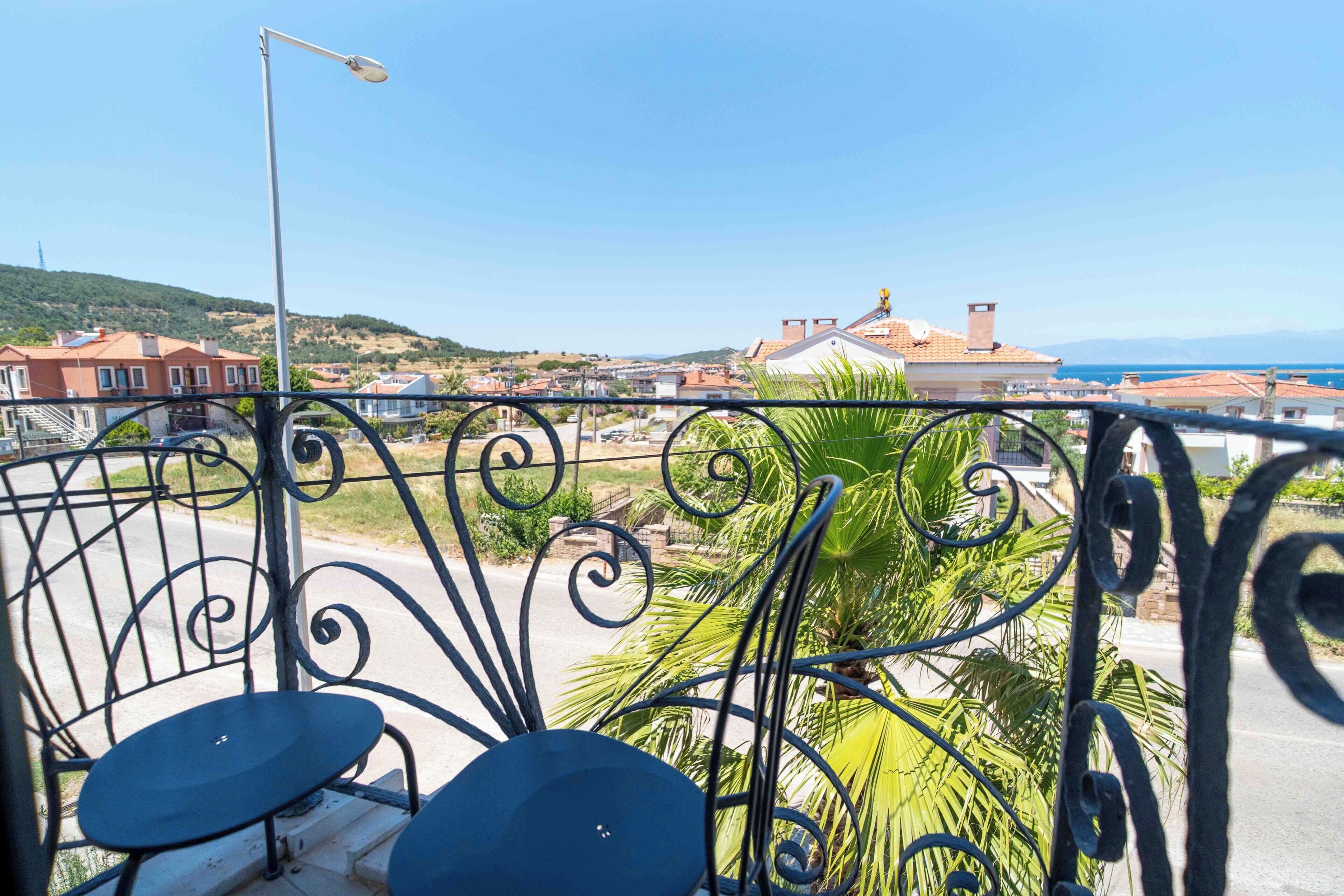Un balcón con barandilla de metal, una farola y vistas a una zona residencial con casas y un paisaje montañoso al fondo.