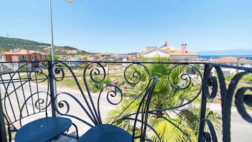 A balcony with a metal railing, a street lamp, and a view of a residential area with houses and a hilly landscape in the background.