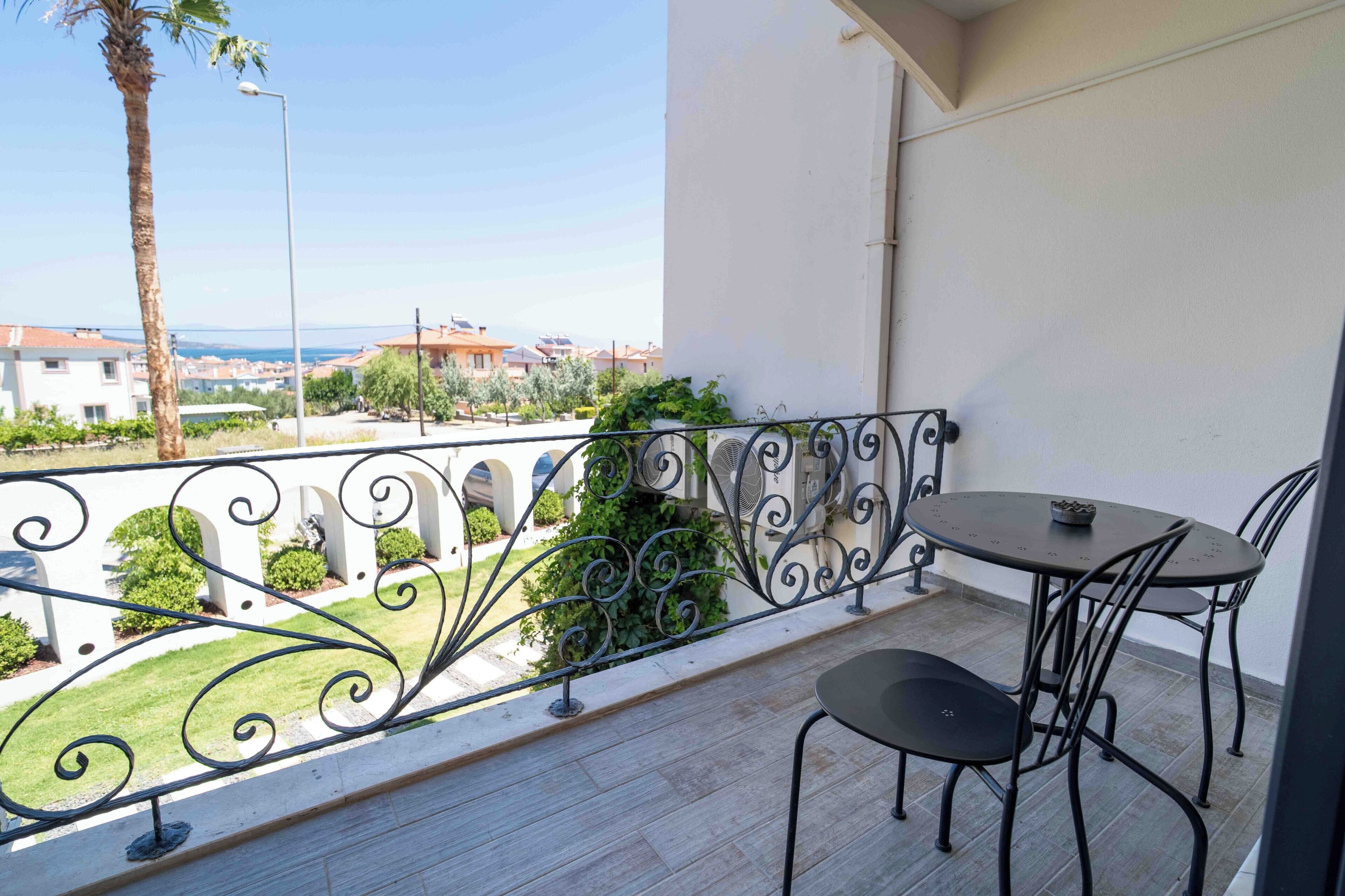 A balcony with a table and chairs, a view of the sea, and a white building in the background.