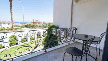 A balcony with a table and chairs, a view of the sea, and a white building in the background.