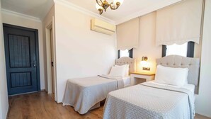 Habitación de hotel con dos camas, una puerta oscura, un equipo de aire acondicionado y un candelabro.
