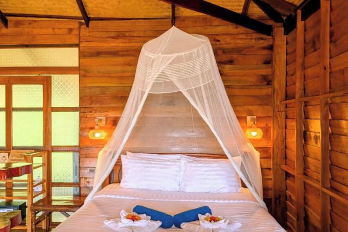 Una habitación de cabaña de madera con una cama bajo una mosquitera, una mesita pequeña y una silla.