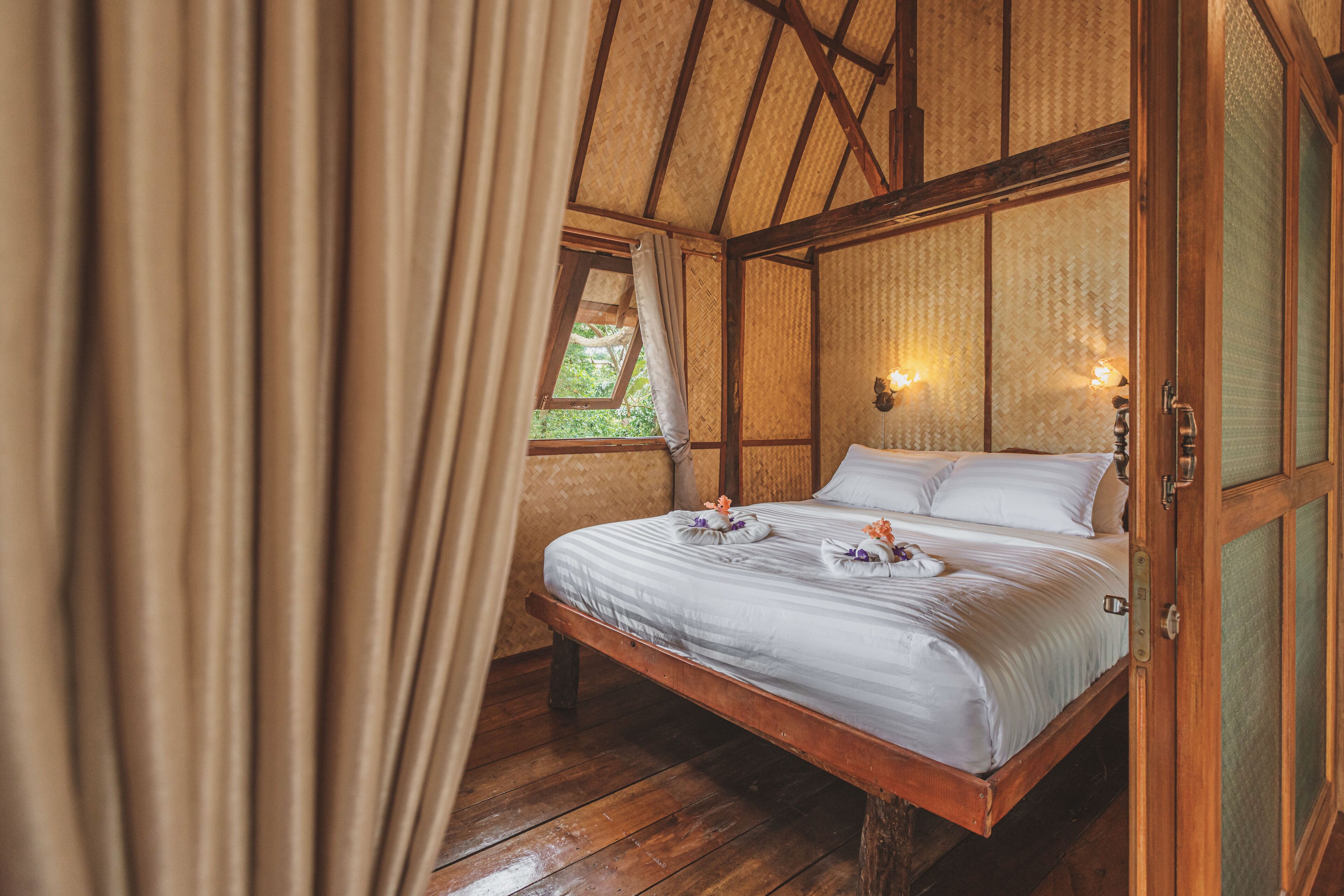 A room with a bed, wooden beams, a window, and a curtain.
