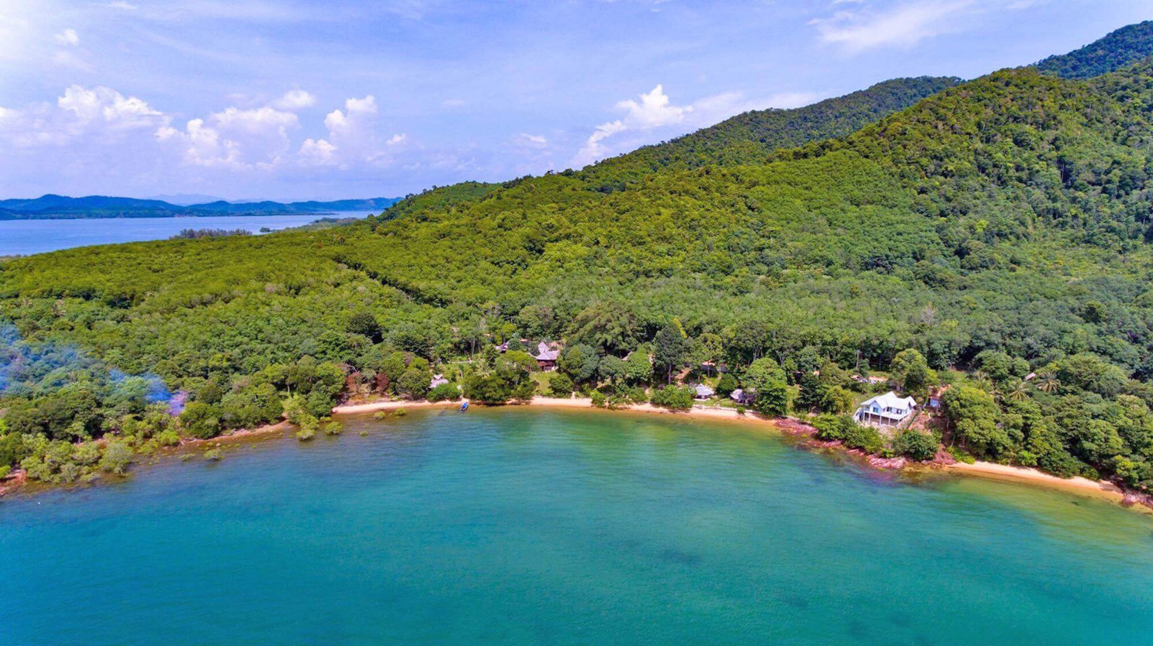 Eine Küstenlandschaft mit Blick auf einen Strand und einen bewaldeten Hügel.