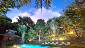 Una piscina rectangular con revestimiento azul claro, rodeada por una terraza de piedra e iluminada con luces cálidas.