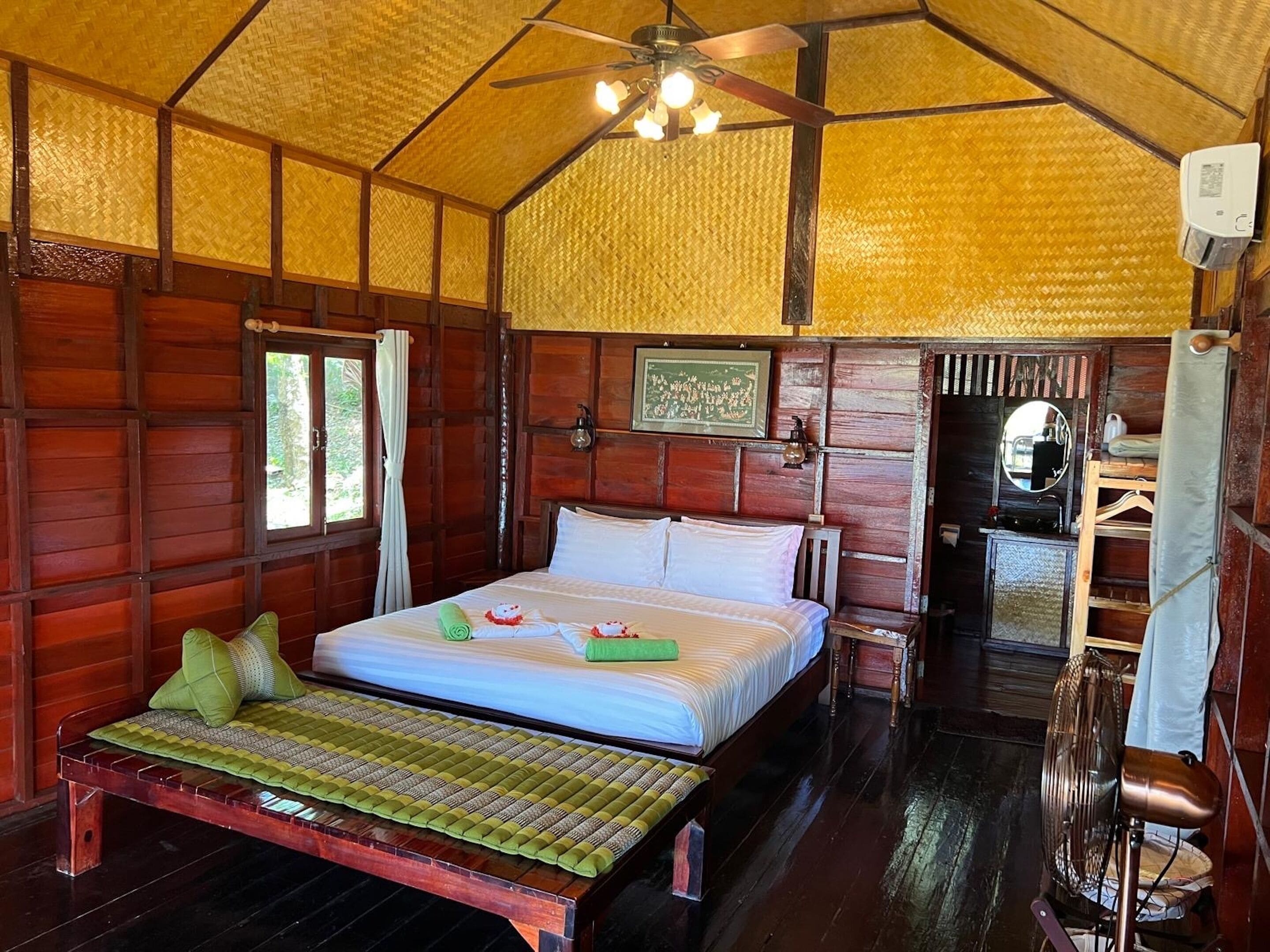 Una habitación con cama, ventilador de techo, espejo y ventana.