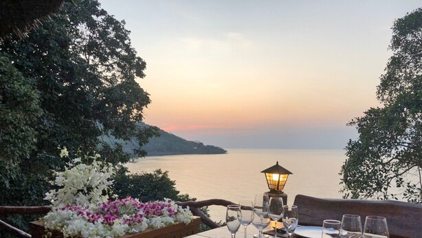 Mesa preparada para la cena con vista al mar al atardecer.
