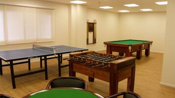 A room with a ping pong table, a foosball table, and a pool table.
