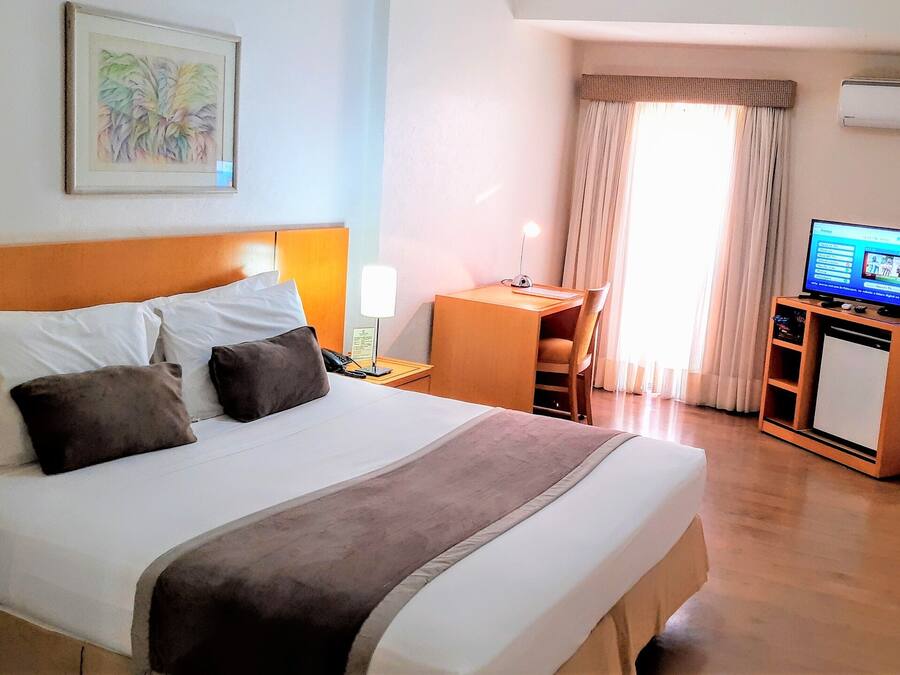 Ein Hotelzimmer mit einem Bett, einem Schreibtisch, einem Sessel, einem Fernseher und einem Fenster mit Vorhängen.