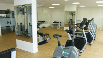 Une salle de sport équipée de matériel d’exercice, notamment des tapis de course, un vélo d’appartement et des appareils de musculation.