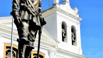 Una estatua de una figura histórica frente a un edificio blanco con un campanario.