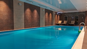 Ein moderner, überdachter Pool mit klarem, blauem Wasser, gefliestem Boden und Liegestühlen an der Wand.