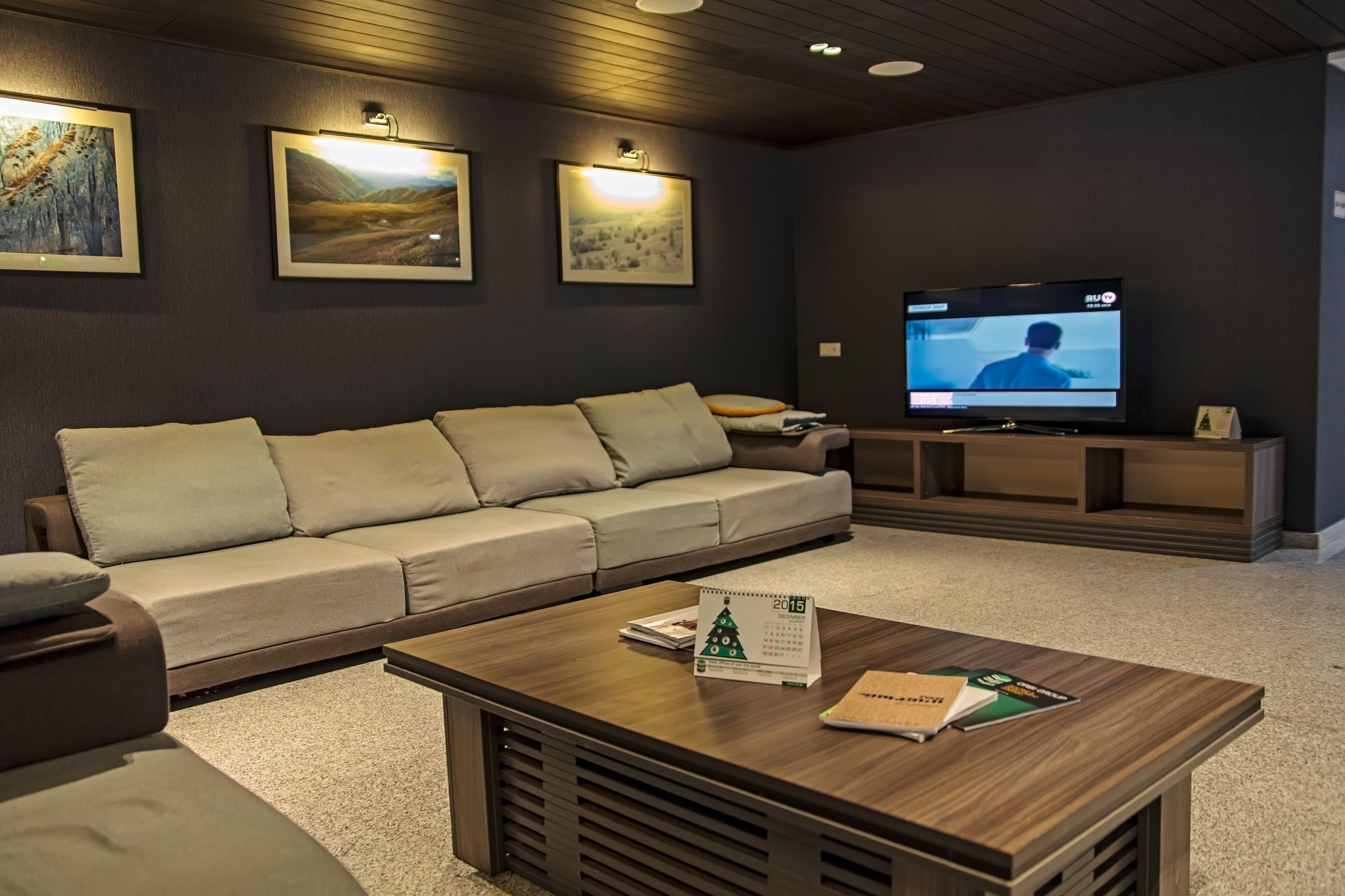 En moderne stue med en beige sofa, et træ sofabord med en kalender og et fladskærms-TV på et stativ.