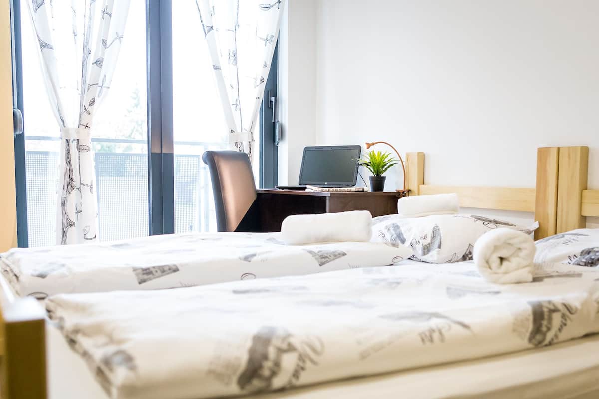 A hotel room with a bed, a desk with a laptop, a chair, and a window with curtains.