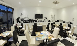 A restaurant with a checkered floor, black and white chairs, tables with travel-themed placemats, and a wall mural of European architecture. - Hostel Moving (Zagreb)