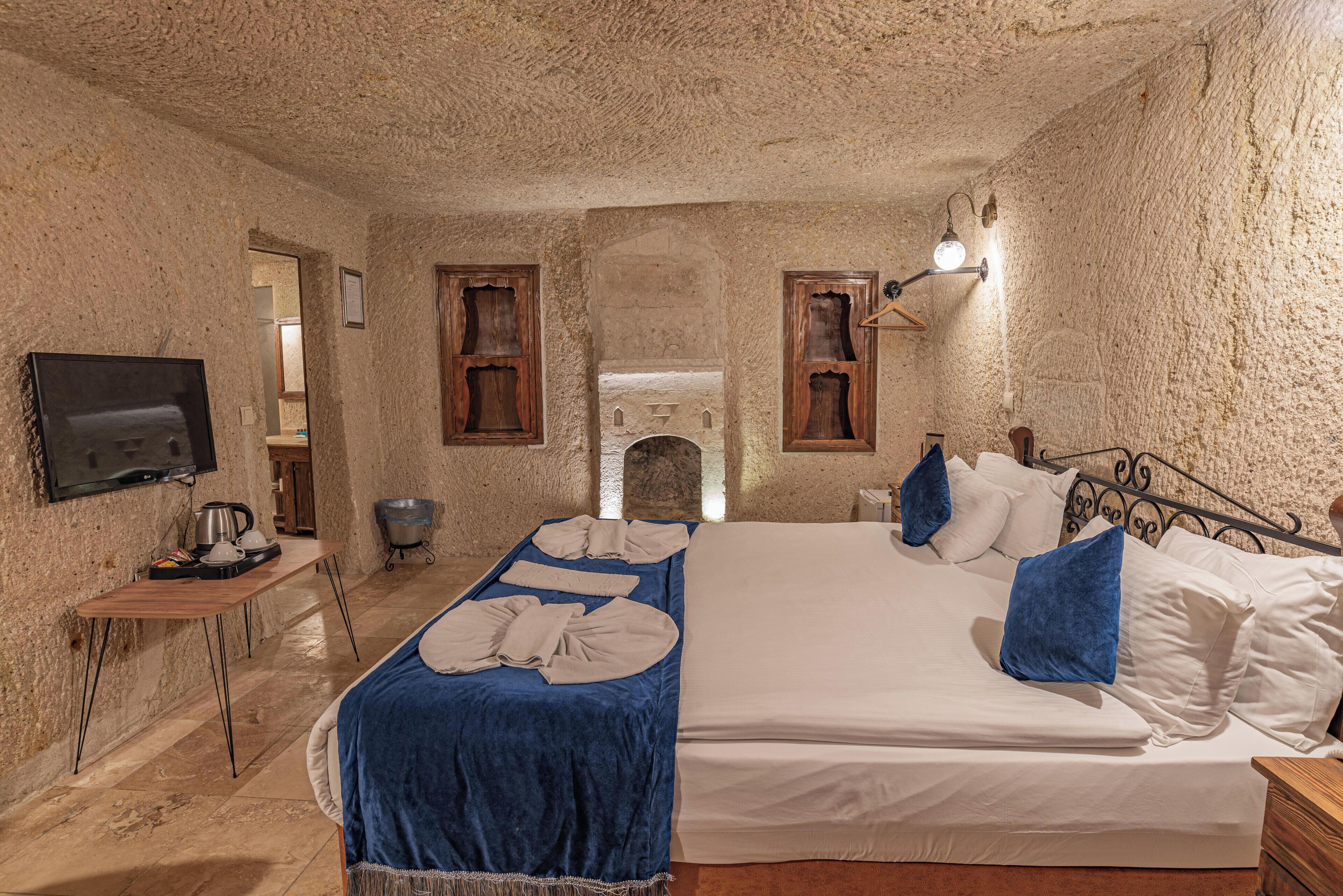 Une chambre avec un lit, un bureau, une télévision et un mur en pierre.