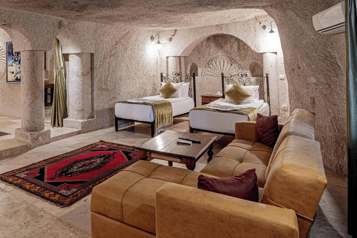 A spacious room with a large bed, a sofa, and a coffee table. There are two archways and a large window.