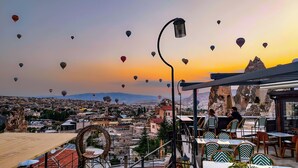 Una terraza en la azotea con mesas y sillas, con vistas a un paisaje urbano que incluye edificios y una montaña al fondo.