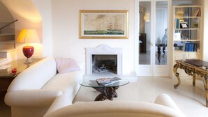 Una sala de estar con un sofá blanco, una mesa de centro de vidrio, una chimenea y una estantería.