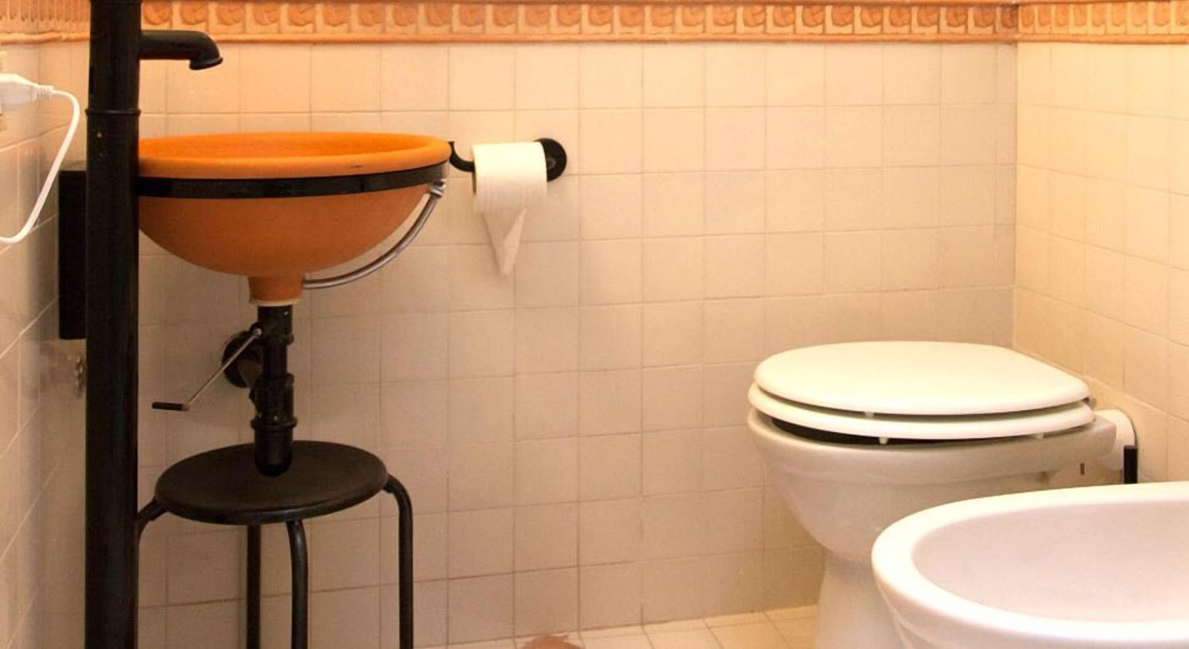 Un baño con inodoro, lavamanos y dispensador de papel higiénico en la pared.