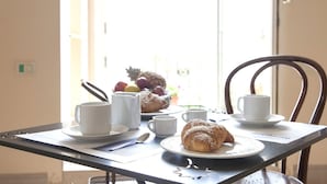Una mesa de desayuno con un croissant, tazas de café y un frutero.
